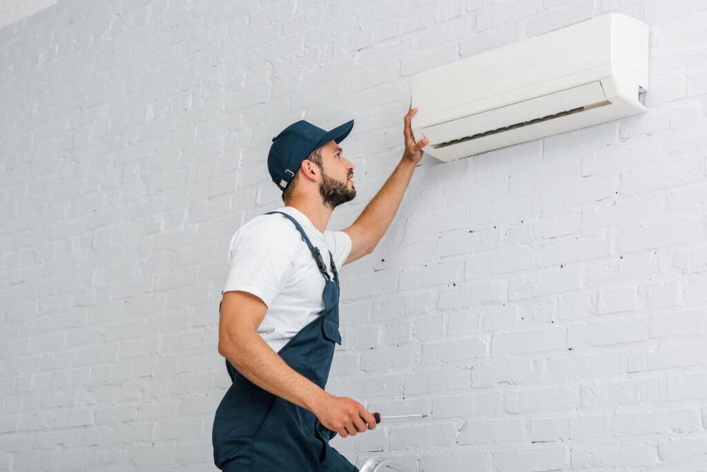 Side view of workman in workwear holding screwdriver near air conditioner